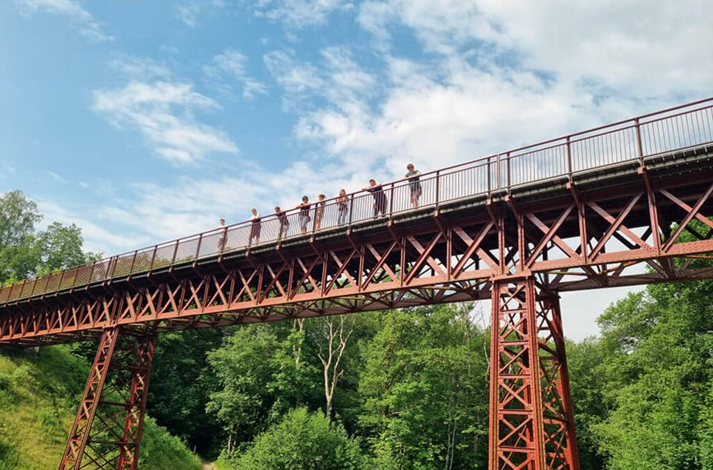 En gruppe unge står på en bro omgivet af grønne træer. De er på udflugt med Fonden Ørtings specialskole for børn og unge med autisme